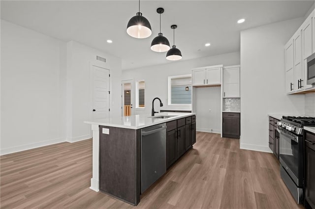 kitchen with stainless steel appliances, white cabinetry, sink, decorative light fixtures, and a kitchen island with sink