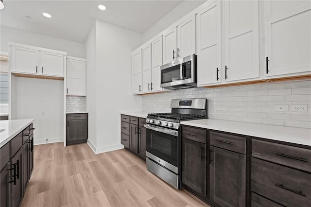 kitchen featuring white cabinets, dark brown cabinets, light wood-type flooring, and appliances with stainless steel finishes