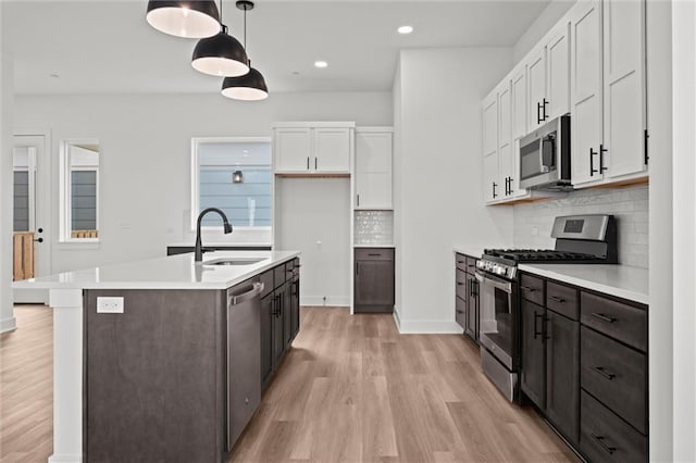 kitchen featuring light hardwood / wood-style flooring, hanging light fixtures, sink, white cabinetry, and appliances with stainless steel finishes