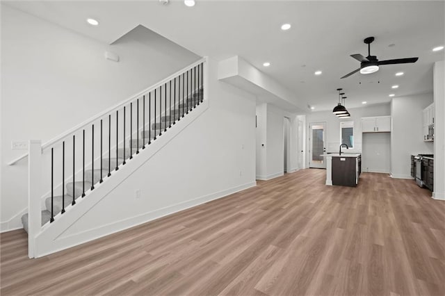 unfurnished living room with ceiling fan, sink, and light hardwood / wood-style flooring