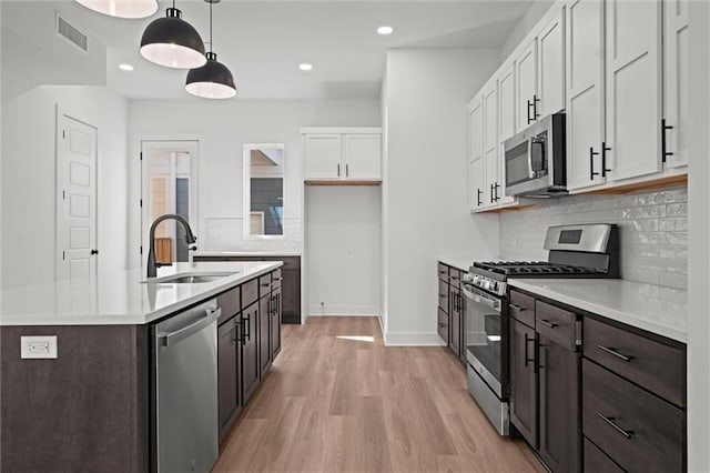 kitchen featuring white cabinetry, appliances with stainless steel finishes, decorative light fixtures, decorative backsplash, and light hardwood / wood-style flooring