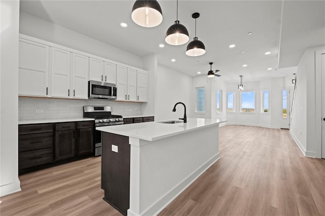 kitchen featuring sink, light wood-type flooring, appliances with stainless steel finishes, and decorative light fixtures