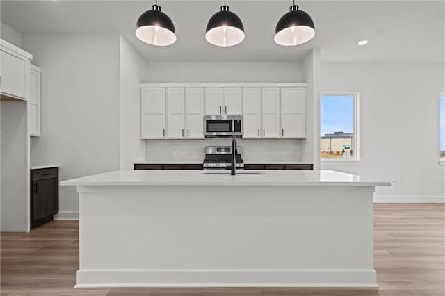 kitchen with backsplash, appliances with stainless steel finishes, decorative light fixtures, and a kitchen island with sink