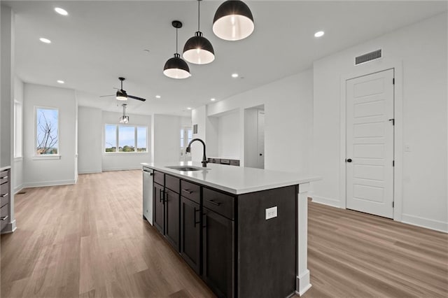 kitchen featuring light hardwood / wood-style floors, sink, decorative light fixtures, a kitchen island with sink, and dishwasher