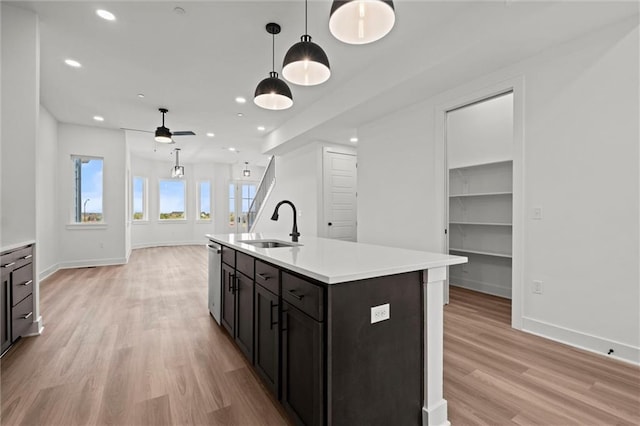 kitchen featuring stainless steel dishwasher, a kitchen island with sink, light hardwood / wood-style flooring, and decorative light fixtures