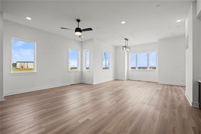 unfurnished living room featuring ceiling fan with notable chandelier, wood-type flooring, and a healthy amount of sunlight