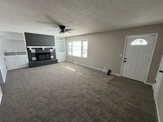 unfurnished living room with dark carpet, a textured ceiling, ceiling fan, and a fireplace