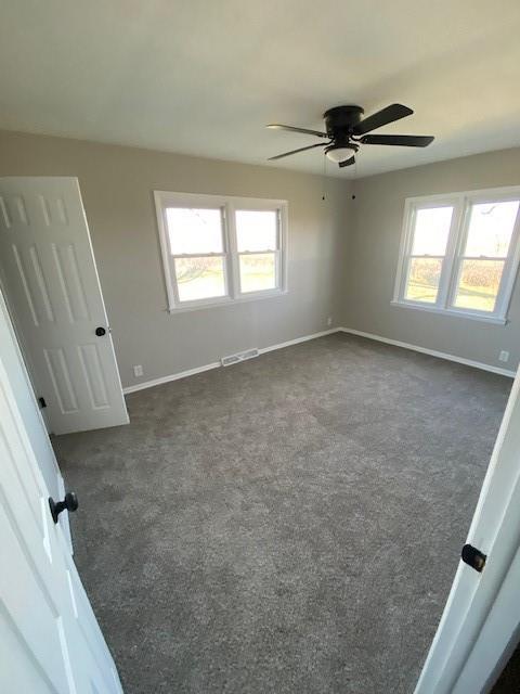 unfurnished room featuring ceiling fan, a healthy amount of sunlight, and dark carpet