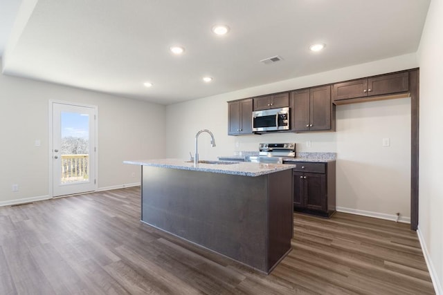 kitchen featuring sink, appliances with stainless steel finishes, dark hardwood / wood-style floors, dark brown cabinetry, and a center island with sink