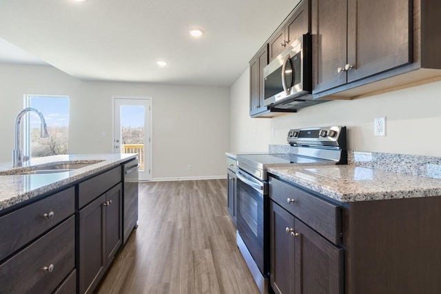 kitchen with dark brown cabinetry, sink, stainless steel appliances, light stone countertops, and hardwood / wood-style floors