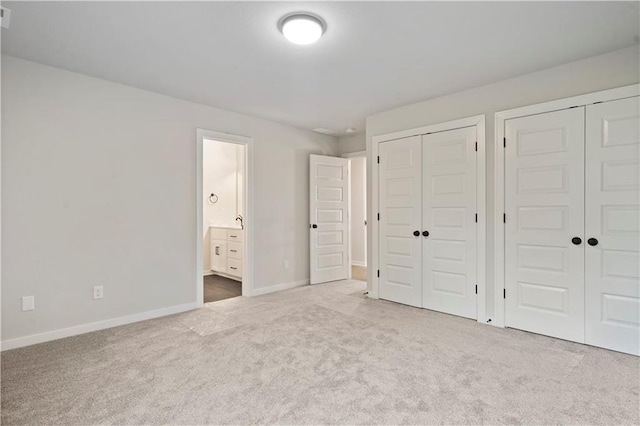 unfurnished bedroom with two closets, carpet flooring, and ensuite bath