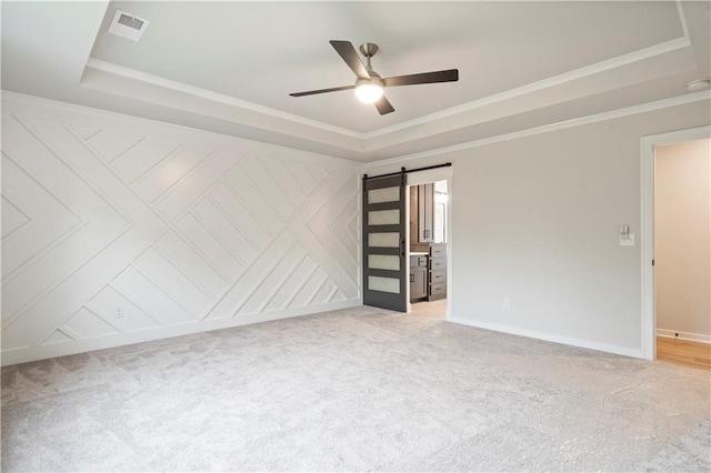 spare room with light carpet, ceiling fan, a barn door, and a tray ceiling