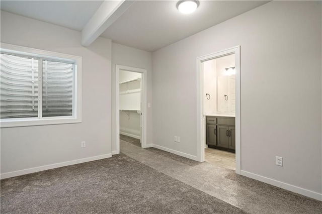 unfurnished bedroom with a closet, carpet flooring, ensuite bath, a spacious closet, and beam ceiling