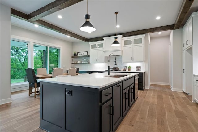 kitchen featuring decorative light fixtures, light hardwood / wood-style flooring, beam ceiling, an island with sink, and white cabinets