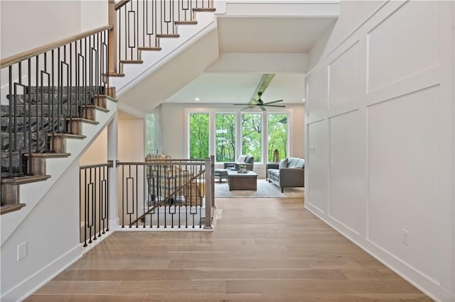 stairway featuring beamed ceiling, ceiling fan, and light wood-type flooring