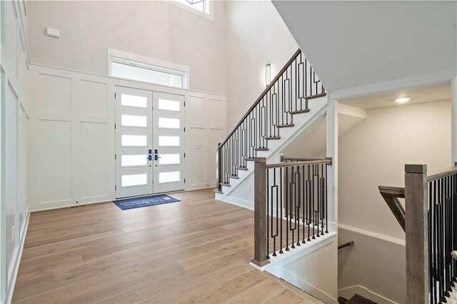 foyer entrance featuring a wealth of natural light, french doors, a towering ceiling, and light wood-type flooring