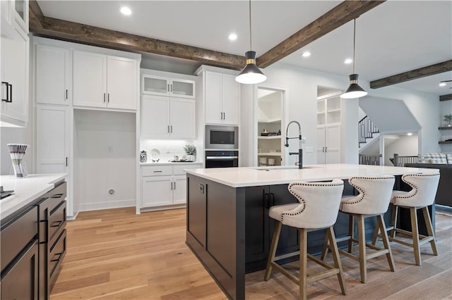 kitchen featuring hanging light fixtures, beamed ceiling, wall oven, light hardwood / wood-style flooring, and stainless steel microwave