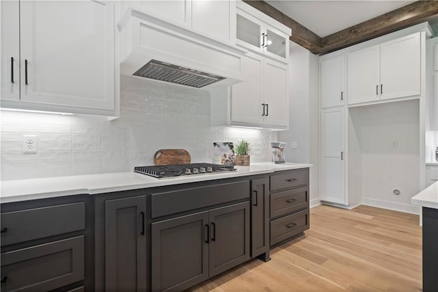 kitchen with backsplash, light hardwood / wood-style flooring, custom exhaust hood, white cabinetry, and beamed ceiling