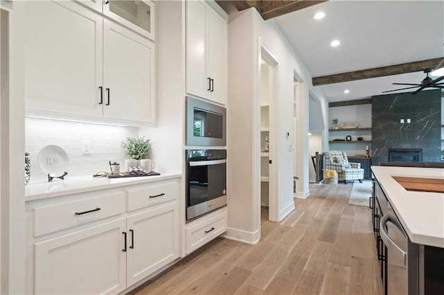 kitchen featuring beamed ceiling, light wood-type flooring, backsplash, stainless steel appliances, and ceiling fan