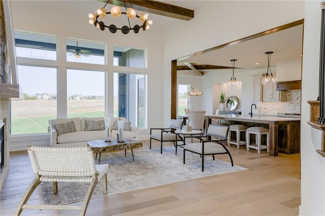 living room featuring an inviting chandelier, sink, beamed ceiling, and light hardwood / wood-style floors