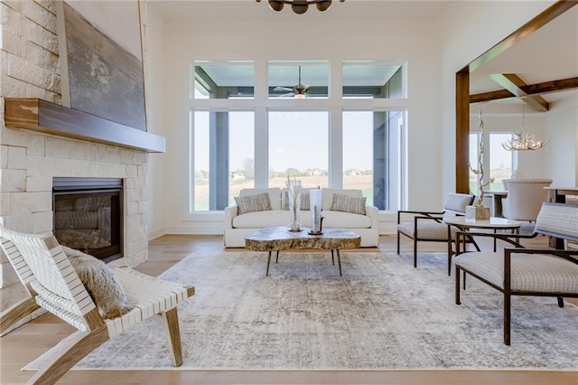 living room featuring a towering ceiling, hardwood / wood-style flooring, a fireplace, and ceiling fan with notable chandelier