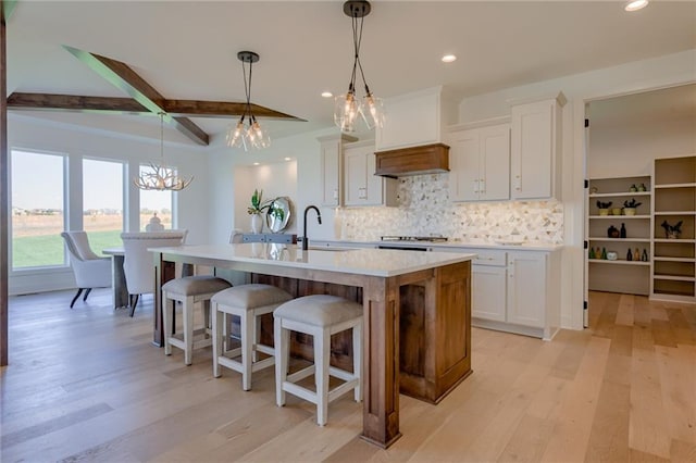 kitchen with light hardwood / wood-style flooring, a center island with sink, custom exhaust hood, white cabinets, and pendant lighting