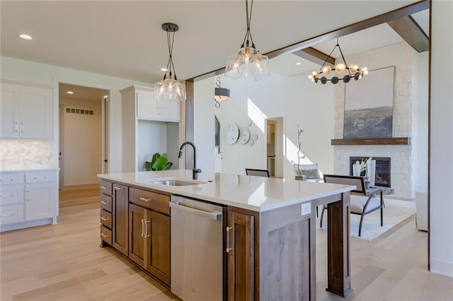 kitchen with light hardwood / wood-style floors, stainless steel dishwasher, white cabinets, a stone fireplace, and sink