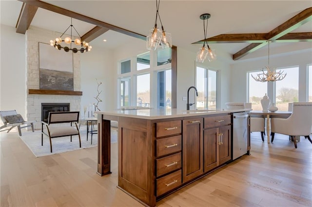 kitchen with an island with sink, light hardwood / wood-style floors, a large fireplace, and pendant lighting