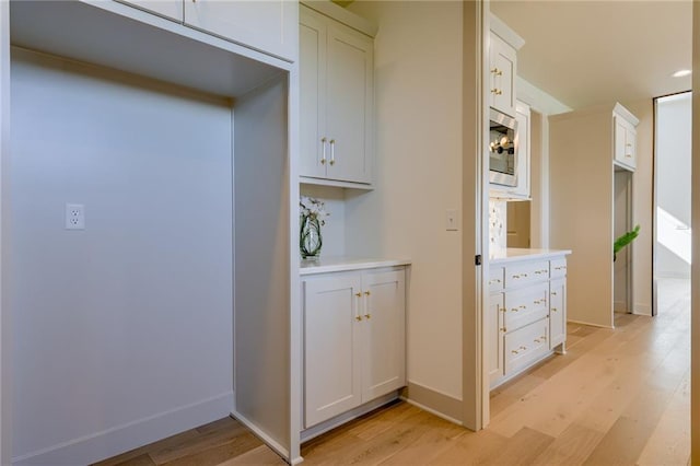 kitchen with white cabinets, stainless steel microwave, and light wood-type flooring