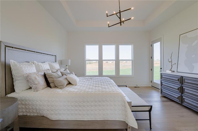 bedroom with an inviting chandelier, a tray ceiling, hardwood / wood-style flooring, and access to outside