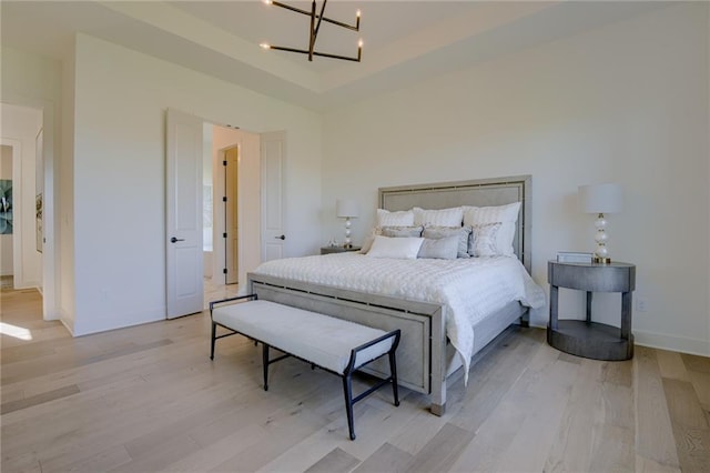 bedroom featuring a notable chandelier, light hardwood / wood-style flooring, and a tray ceiling