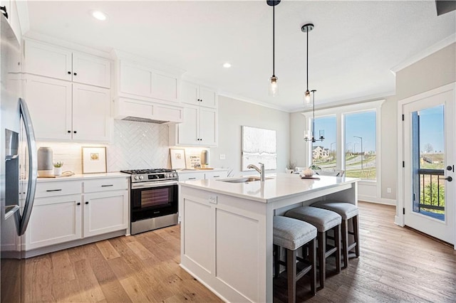 kitchen featuring sink, decorative light fixtures, appliances with stainless steel finishes, an island with sink, and white cabinets