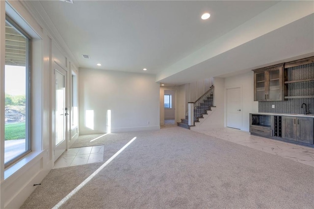 unfurnished living room featuring sink, light carpet, and a healthy amount of sunlight