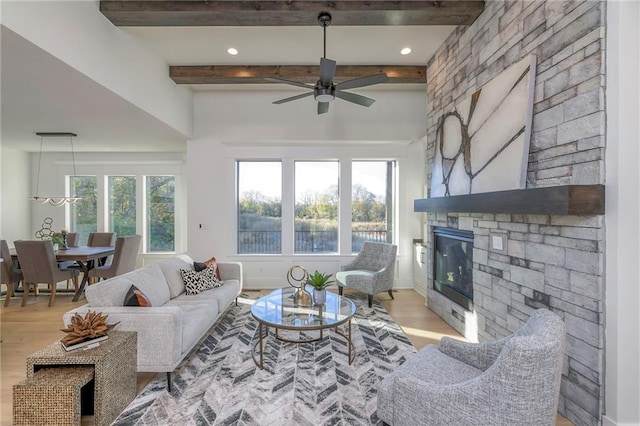 living room featuring light hardwood / wood-style floors, ceiling fan, a stone fireplace, and beam ceiling