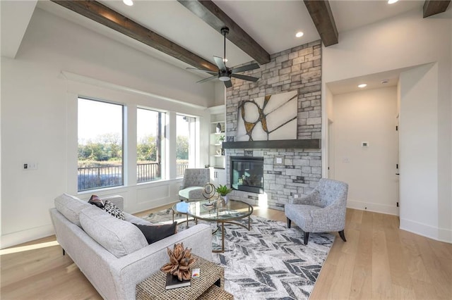 living room with a fireplace, beam ceiling, ceiling fan, and light hardwood / wood-style flooring