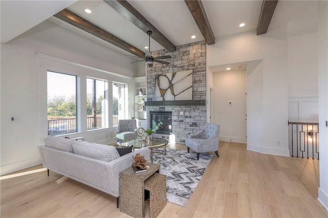 living room with light hardwood / wood-style floors, beam ceiling, ceiling fan, and a fireplace