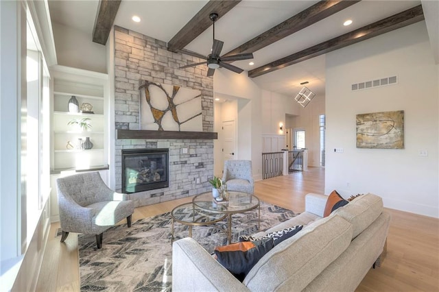 living room with beamed ceiling, a stone fireplace, light hardwood / wood-style floors, and built in features