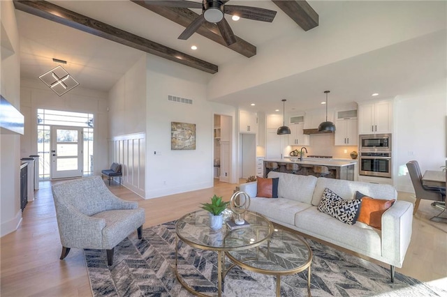 living room featuring sink, beamed ceiling, a towering ceiling, and light wood-type flooring