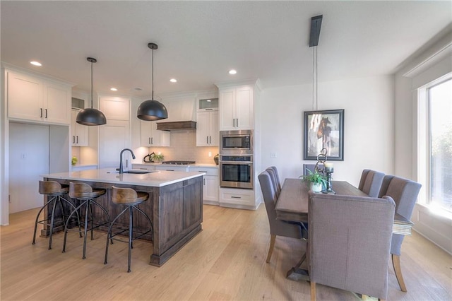 kitchen featuring a center island with sink, hanging light fixtures, sink, appliances with stainless steel finishes, and white cabinets