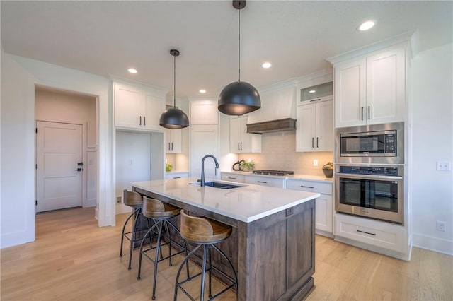 kitchen with sink, premium range hood, stainless steel appliances, white cabinets, and a kitchen island with sink