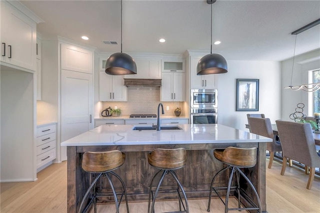 kitchen with sink, a kitchen island with sink, white cabinetry, and pendant lighting