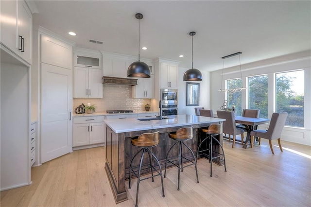 kitchen featuring a center island with sink, hanging light fixtures, white cabinets, and stainless steel appliances