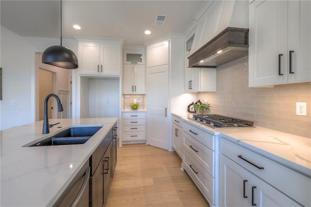 kitchen with white cabinetry, hanging light fixtures, premium range hood, sink, and light stone counters