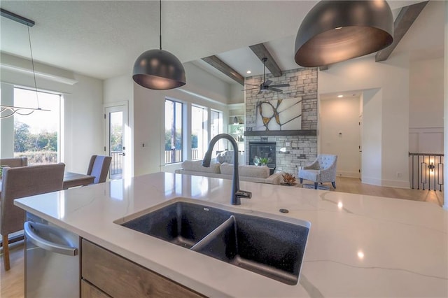 kitchen featuring hanging light fixtures, light stone countertops, plenty of natural light, a stone fireplace, and sink