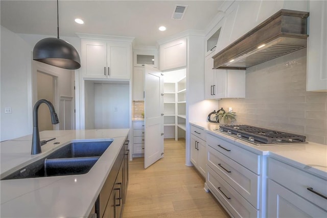 kitchen with white cabinetry, premium range hood, sink, light stone counters, and pendant lighting