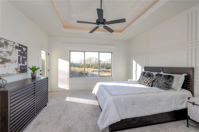 bedroom with ceiling fan, a tray ceiling, and light colored carpet