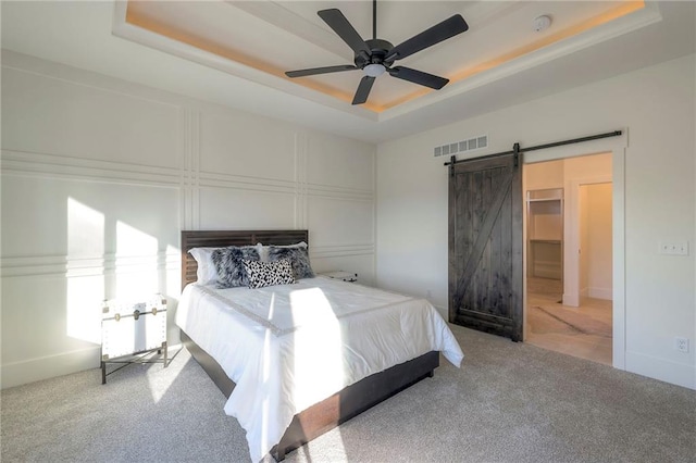 carpeted bedroom featuring a tray ceiling, ceiling fan, and a barn door