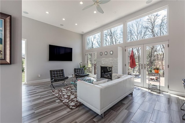 living room featuring a stone fireplace, plenty of natural light, a high ceiling, and ceiling fan