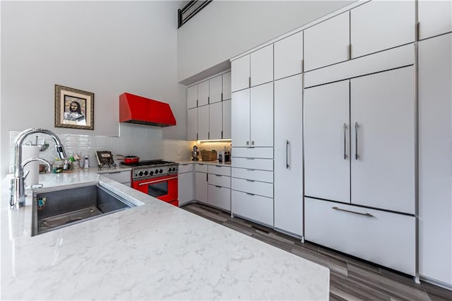 kitchen featuring dark hardwood / wood-style floors, tasteful backsplash, double oven range, premium range hood, and sink