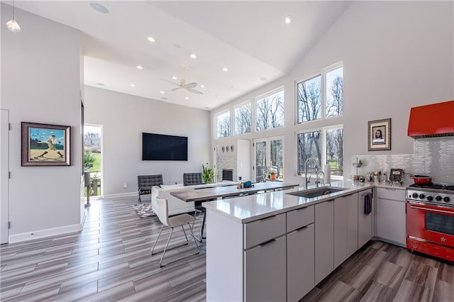 kitchen featuring kitchen peninsula, gas range, tasteful backsplash, high vaulted ceiling, and sink